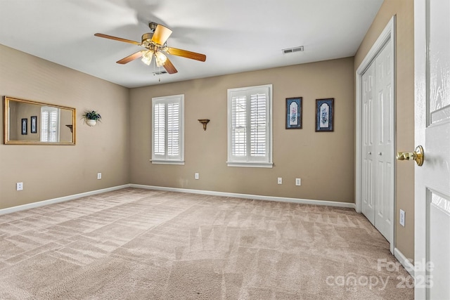 unfurnished room featuring baseboards, visible vents, a ceiling fan, and light colored carpet