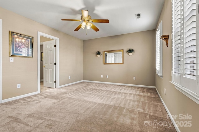 empty room featuring a ceiling fan, light colored carpet, visible vents, and baseboards