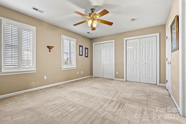 unfurnished bedroom with light carpet, a ceiling fan, visible vents, baseboards, and two closets