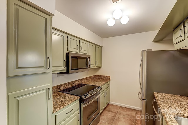 kitchen featuring light tile patterned floors, appliances with stainless steel finishes, dark stone countertops, and baseboards