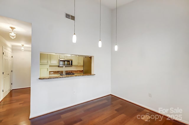 kitchen featuring stone countertops, wood finished floors, cream cabinetry, stainless steel microwave, and pendant lighting