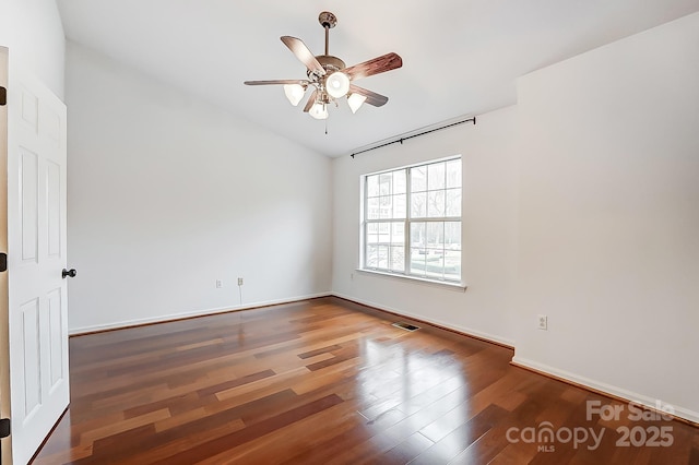 empty room with wood finished floors, visible vents, a ceiling fan, vaulted ceiling, and baseboards