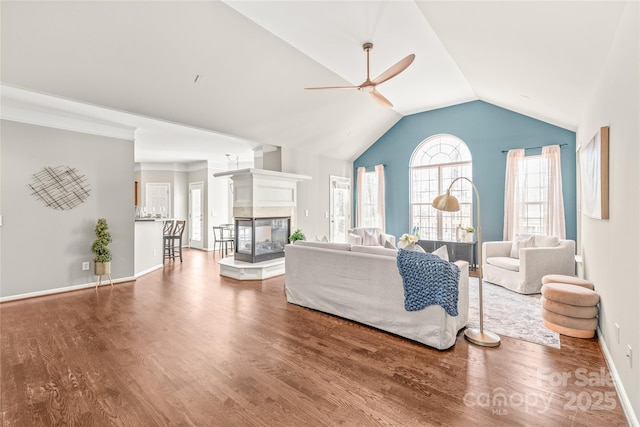 living room with ceiling fan, vaulted ceiling, wood-type flooring, and a multi sided fireplace