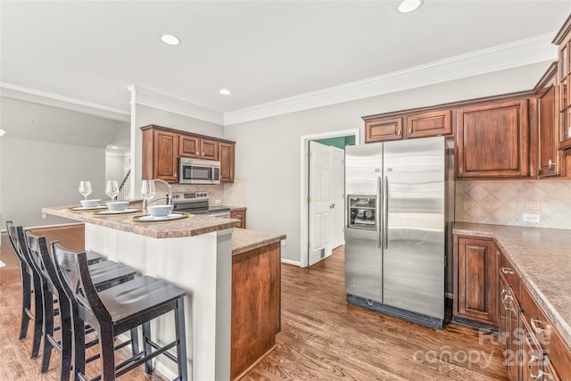 kitchen featuring stainless steel appliances, decorative backsplash, a breakfast bar, dark hardwood / wood-style floors, and crown molding