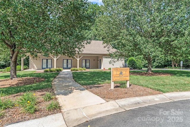 view of property hidden behind natural elements featuring french doors and a front lawn