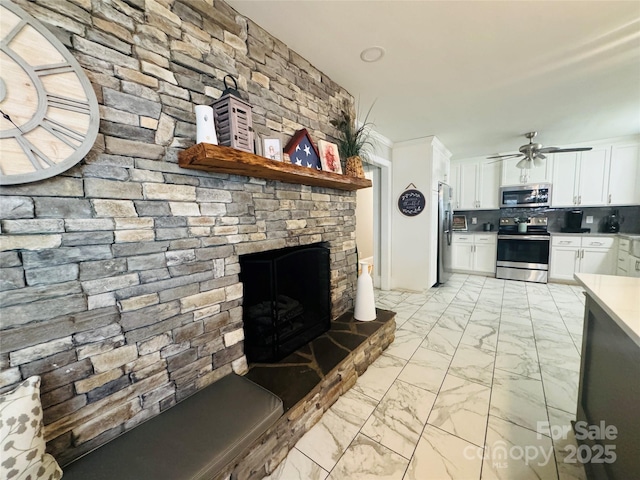 kitchen featuring white cabinetry, a large fireplace, backsplash, ceiling fan, and stainless steel appliances