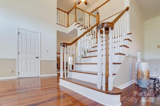 stairway featuring crown molding, a towering ceiling, baseboards, and wood finished floors