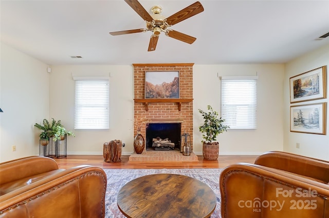 living area featuring a brick fireplace, a healthy amount of sunlight, and wood finished floors