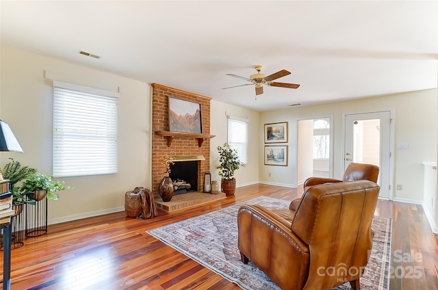 living room with a fireplace, visible vents, a ceiling fan, wood finished floors, and baseboards