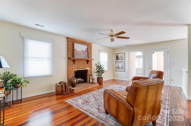 living room featuring a fireplace, wood finished floors, a ceiling fan, visible vents, and baseboards