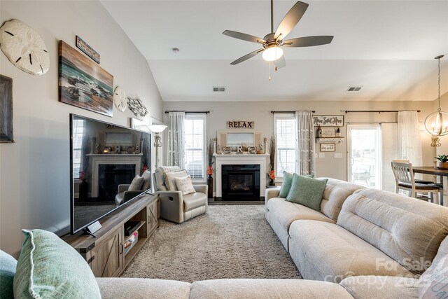 living area with visible vents, vaulted ceiling, a glass covered fireplace, and ceiling fan with notable chandelier