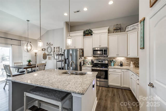 kitchen with vaulted ceiling, a sink, decorative backsplash, appliances with stainless steel finishes, and dark wood-type flooring