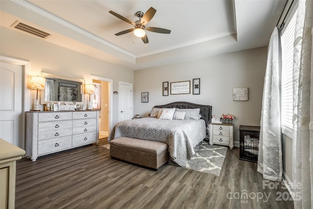 bedroom with crown molding, visible vents, dark wood-type flooring, and a tray ceiling