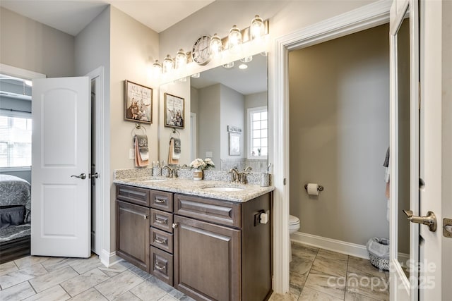 ensuite bathroom featuring connected bathroom, toilet, baseboards, and a sink