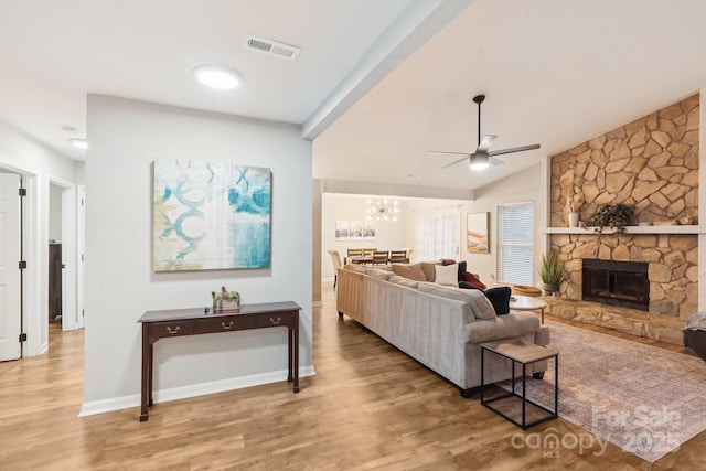 living area featuring light wood finished floors, visible vents, vaulted ceiling, a stone fireplace, and ceiling fan with notable chandelier