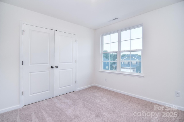 unfurnished bedroom with a closet, light colored carpet, visible vents, and baseboards