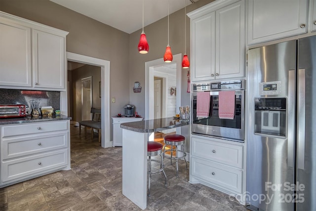 kitchen with white cabinetry, appliances with stainless steel finishes, dark stone counters, and hanging light fixtures