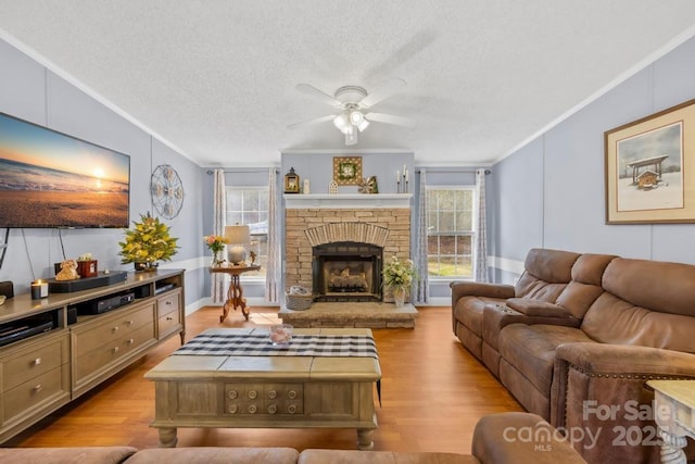 living room with a fireplace, ceiling fan, light hardwood / wood-style floors, a textured ceiling, and ornamental molding