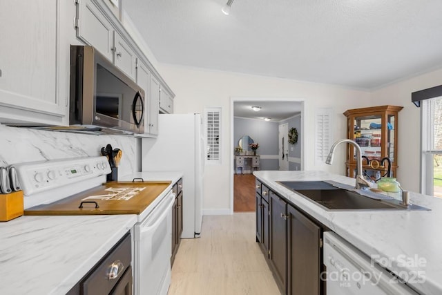 kitchen with decorative backsplash, light wood-type flooring, white appliances, sink, and light stone countertops