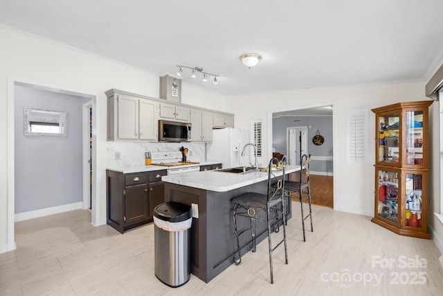 kitchen featuring a center island with sink, backsplash, a kitchen breakfast bar, white appliances, and sink