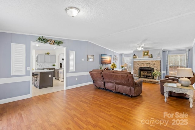 living room with ceiling fan, vaulted ceiling, light wood-type flooring, and a stone fireplace