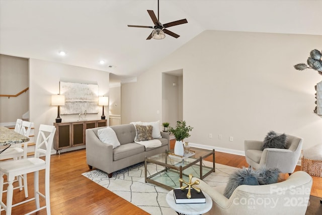 living room featuring ceiling fan, baseboards, vaulted ceiling, light wood-style floors, and stairway