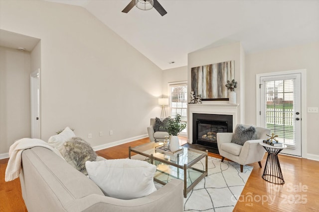 living room featuring lofted ceiling, a ceiling fan, baseboards, light wood-style floors, and a glass covered fireplace