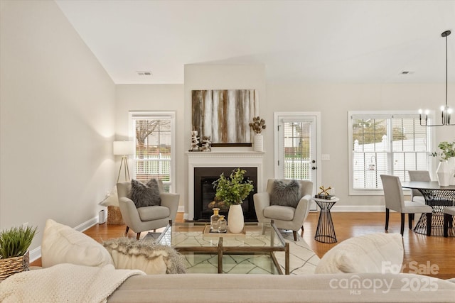 living room with a glass covered fireplace, wood finished floors, baseboards, and an inviting chandelier