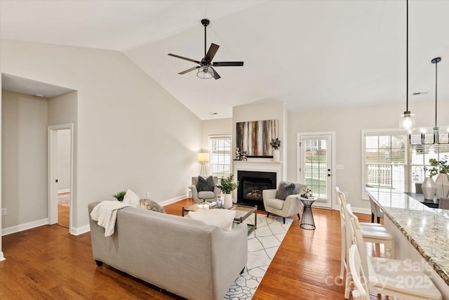 living area featuring visible vents, baseboards, a ceiling fan, a glass covered fireplace, and light wood-style flooring