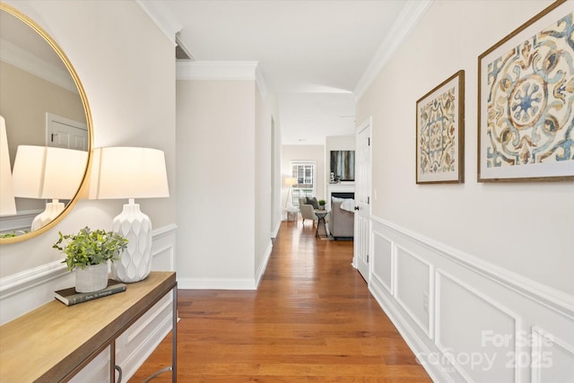 corridor with a wainscoted wall, a decorative wall, wood finished floors, and crown molding