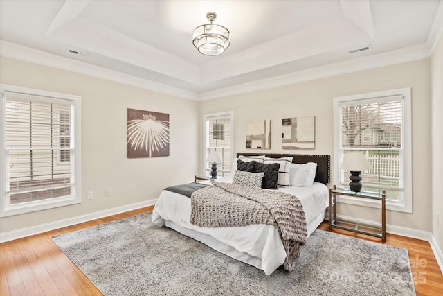 bedroom with baseboards, visible vents, a raised ceiling, and wood finished floors