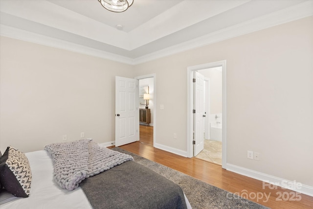 bedroom with a tray ceiling, ensuite bath, wood finished floors, and baseboards