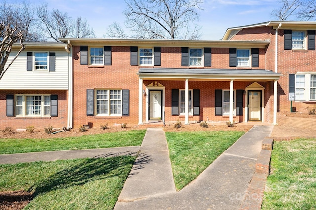 townhome / multi-family property with covered porch, a front yard, and brick siding