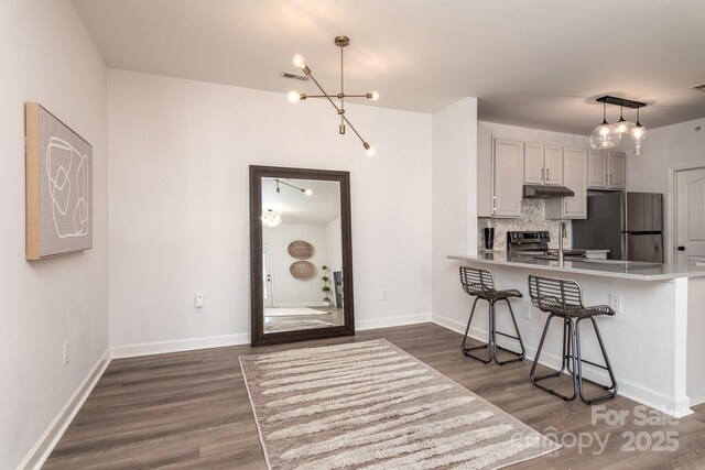 kitchen with white cabinets, stainless steel fridge, a kitchen bar, hanging light fixtures, and kitchen peninsula