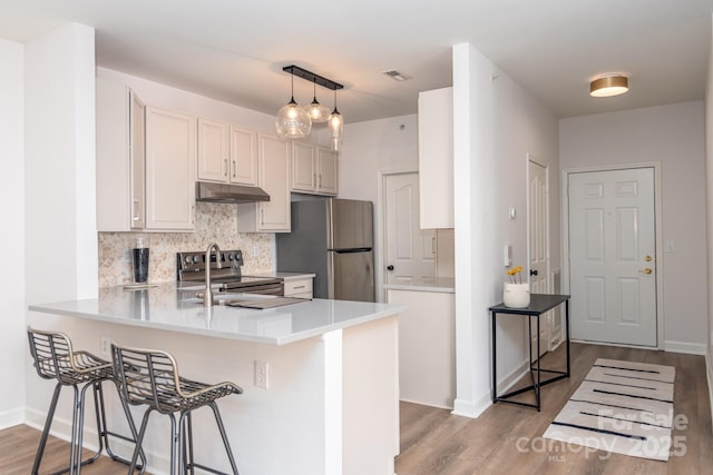 kitchen with a kitchen bar, appliances with stainless steel finishes, kitchen peninsula, pendant lighting, and backsplash