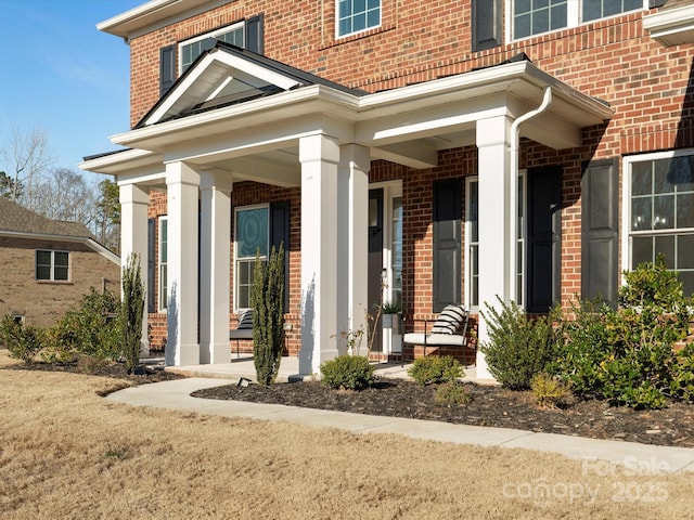 doorway to property featuring a porch and brick siding