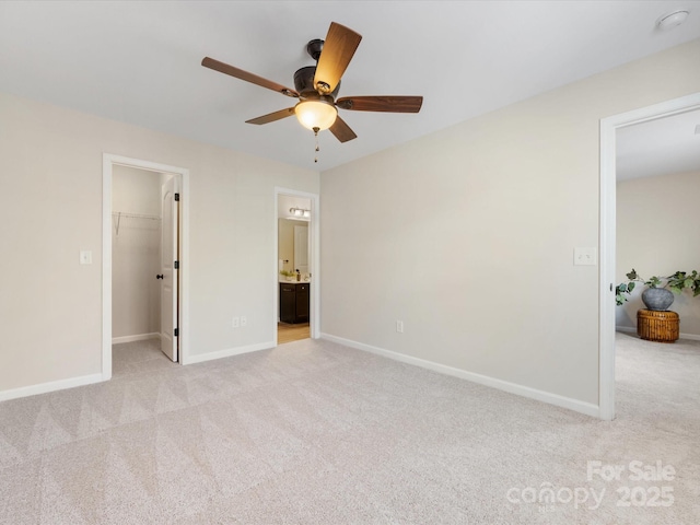 unfurnished bedroom with a closet, a walk in closet, ceiling fan, connected bathroom, and light carpet