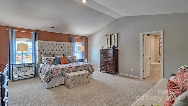 bedroom with light colored carpet, connected bathroom, vaulted ceiling, and multiple windows