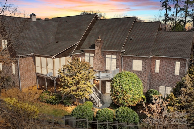 back of house with a balcony, a chimney, stairs, fence, and brick siding