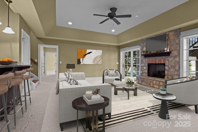 living room featuring light carpet, a raised ceiling, a ceiling fan, a fireplace, and recessed lighting