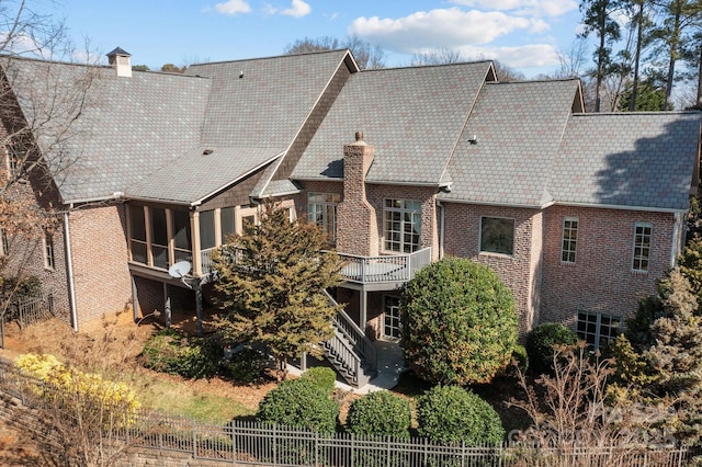 rear view of property with brick siding, a chimney, fence, and a sunroom