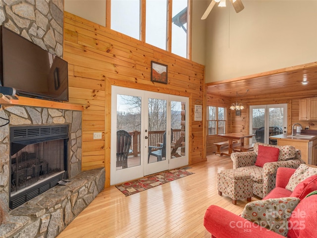 living room with a stone fireplace, ceiling fan with notable chandelier, light wood-type flooring, and wood walls