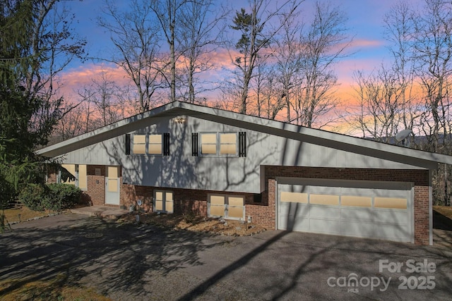 split level home featuring driveway, an attached garage, and brick siding