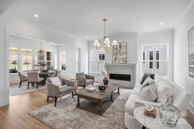 living area featuring wood finished floors, crown molding, a fireplace, a notable chandelier, and recessed lighting