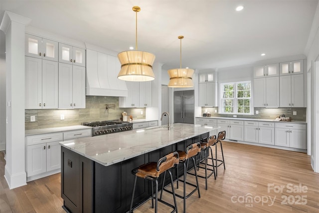 kitchen featuring custom exhaust hood, stove, light wood-style floors, a sink, and stainless steel built in refrigerator