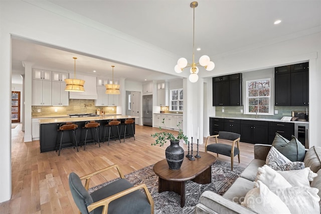 living room with wine cooler, ornamental molding, light wood-type flooring, a notable chandelier, and recessed lighting