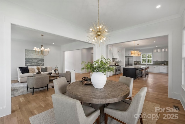 dining room with light wood-type flooring, crown molding, and a notable chandelier