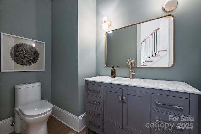 half bath with toilet, baseboards, wood finished floors, and vanity