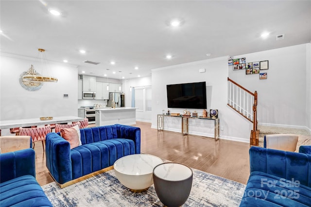 living area with recessed lighting, visible vents, light wood-style floors, ornamental molding, and stairs