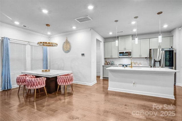 kitchen with stainless steel appliances, light countertops, hanging light fixtures, visible vents, and an island with sink